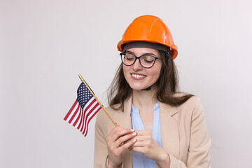 A girl in a construction helmet and an American flag stands happy on a white background.