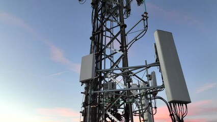 Cell tower with multiple 5G, 4G & LTE antennas and radio dishes. Close-up video from drone with tower against evening sky.