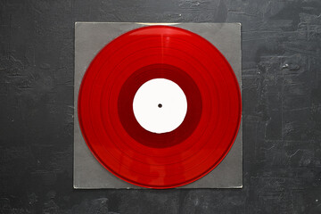 Aged black paper cover and red vinyl LP record isolated on stone background	
