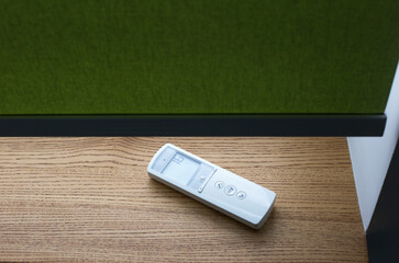 White remote control panel for motorized roller shades or automatic blinds lies on a wooden...