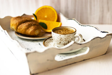 Morning breakfast coffee cup on saucer, croissant, fresh orange fruit on white shabby wooden tray