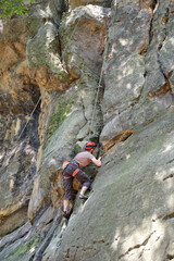 Strong male climber climbing steep wall of rocky mountain. Sportsman overcoming difficult route. Engaging in extreme sports hobby concept