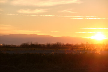 Beautiful evening panoramic landscape with bright setting sun over distant mountain peaks and asphalt road in front at sunset