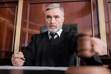 senior judge in mantle holding blurred gavel while sentencing in court