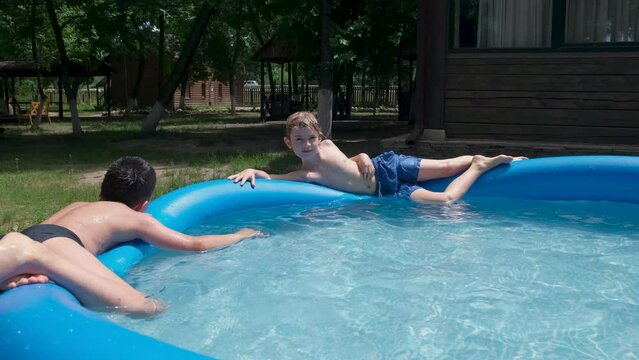 Boys splashing in the swimming pool. Children enjoying summer vacation. Happy fun loving group of friends playing and relaxing at a pool party in summer sunny day. Slow motion. 