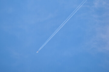 Distant passenger jet plane flying on high altitude on clear blue sky leaving white smoke trace of contrail behind. Air transportation concept