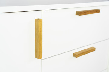 Furniture handles on white chest drawer for bedroom.  Furniture fittings from natural oak wood in modern eco style.