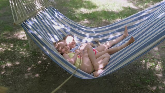 Small girls enjoying summertime outdoors. Children lying in a hammock on camping. Smiling, laughing. Happiness, togethreness concept.