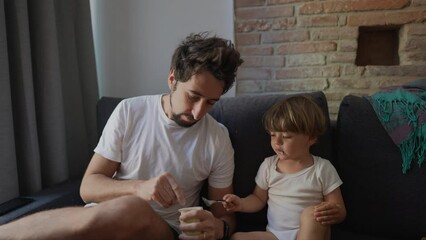 Father feeding yogurt to son candid dad feeds food to child