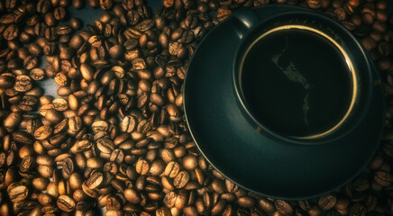 Top view of a cup of espresso on a black background and roasted coffee beans underneath. Background concept