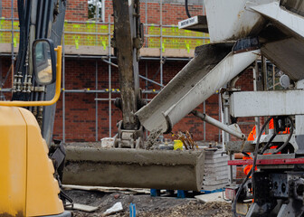 Exavator bucket filled with wet concrete to bring it to plce of concrete works on building site