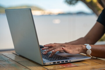 Hands of a woman working with her laptop at home with a beautiful view from her backyard