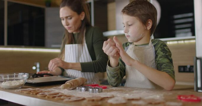 Young family mother and son making home-made cookies at kitchen table working with dough smiling talking. Healthy food, lifestyle and parenthood concept. Slow motion
