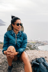 Woman relaxing during a hike. Young female wearing sunglasses sitting on a cliff.