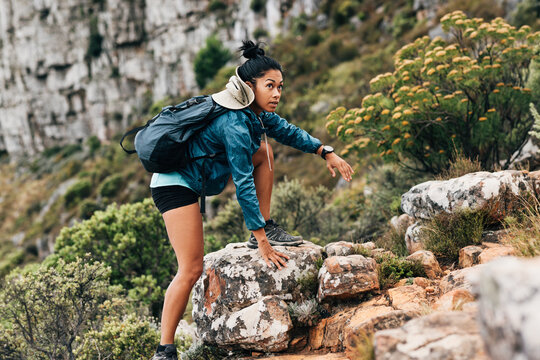 Woman hiker climbing up on a rock. Young female in sports clothes with backpack hiking on mountain terrain.