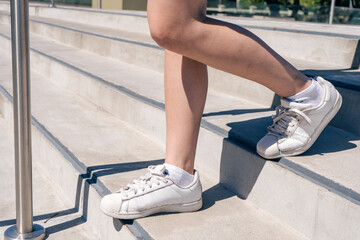 Beautiful Legs of a Caucasian or Hispanic woman in white sneakers walking down a concrete stairs. Horizontal orientation.