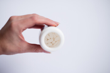 Female hand holding a bottle of white tablets on light background. Selective focus inside the bottle on pills. Medical treatment and pharmacy concept. 