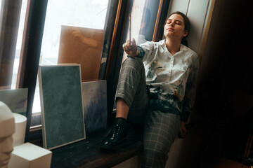 A young girl artist sits on a windowsill by the window