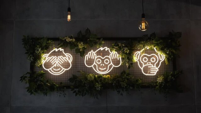 Neon sign in the restaurant. Three cute monkeys light up the room. Neon is decorated with leaves and flowers.