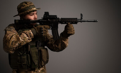 Portrait of  soldier in military camouflage uniform protected with helmet, body armor, holding machine gun desaturated on a gray background. Army. Sniper. Soldier shooting. Military Conflict Actions.