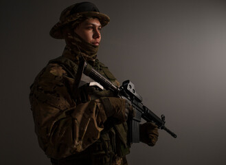 Soldier in a military camouflage uniform wearing a  helmet, body armor, and holding a machine gun on a gray background.  Sniper. Army banner.   Military Conflict Actions. Man In Camouflage.