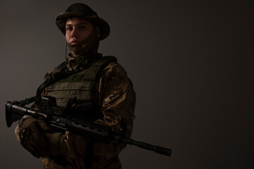 Fototapeta premium Soldier in a military camouflage uniform wearing a helmet, body armor, and holding a machine gun on a gray background. Sniper. Army banner. Military Conflict Actions. Man In Camouflage.