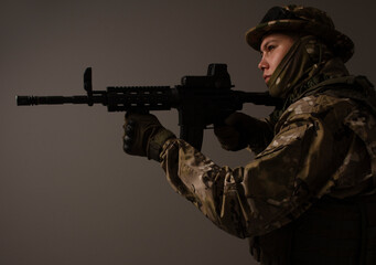 Fototapeta premium Portrait of soldier in military camouflage uniform protected with helmet, body armor, holding machine gun desaturated on a gray background. Army. Sniper. Soldier shooting. Military Conflict Actions.
