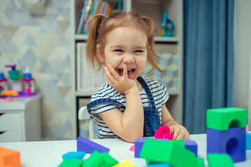 The little girl plays with colorful toy blocks and builds a tower. Educational and creative toys...