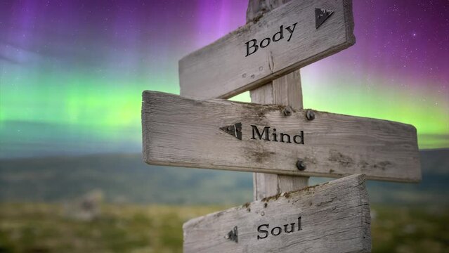 Body mind and soul text quote on wooden signpost outdoors in nature with aurora borealis. Personal development concept.