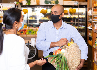 Family couple in protective mask choosing groceries together in supermarket