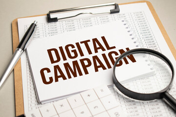 On the table are reports, a magnifying glass, a calculator, and a white notepad with the words DIGITAL CAMPAIGN . Business concept