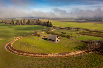 Classic Wooden Barn Surrounded By An Irrigation Ditch. Aerial drone view of this old structure on a foggy winter day in the agricultural Skagit Valley, Washington. 