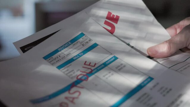 A closeup view of a Caucasian man holding past due notices of some of his bills.