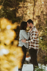 Fototapeta premium Beautiful couple hugging between snowy pines, woman in casual clothes holding hands on man chest. Selective focus
