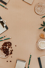 Top view brown neutral workspace office desk with coffee and office supplies. Flat lay work table with craft notebook, green olive leaf and supplies. Home blogger