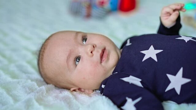 Nice little baby boy in black shirt with stars on bed. Portrait of a calm cute child looking up. Close up. Blurred backdrop.