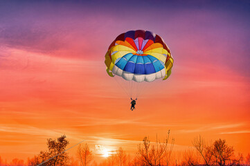 Gliding with a parachute on the background of bright sunset.