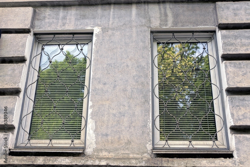 Wall mural two white windows with a iron lattice on a gray concrete wall in the street