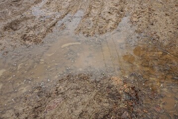 part of a rural road of brown earth with a large pothole and frozen muddy water in the ice