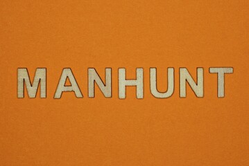 gray word manhunt made of wooden letters on brown background