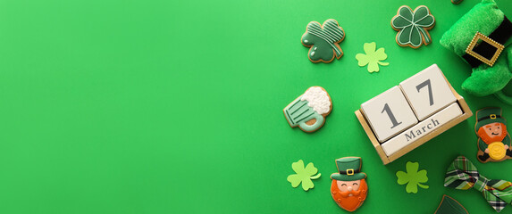 Composition with tasty gingerbread cookies and calendar with date of St. Patrick's Day on green background with space for text