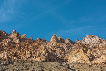 Scenic mountain landscape with sharp rocks under blue sky in sunny day. Colorful scenery with gold sunlit sharp rocky mountains. Sharp rocks in bright sun. High rocky mountains in golden sunlight.