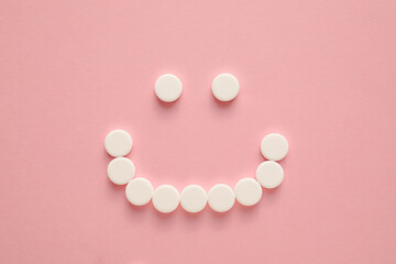 Smile made of white pills on color background