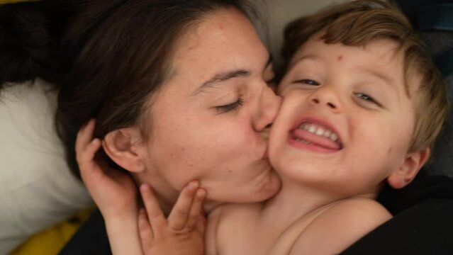 Mother kissing toddler boy on cheek playful mom kisses child