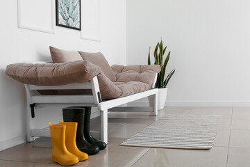Rubber boots and sofa near white wall in hallway
