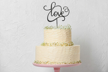 Dessert stand with beautiful wedding cake and word LOVE on light background