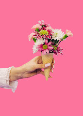 Female hand holding Ice cream waffle cornet with pastel pink roses and other various flowers over light pastel background. Valentines or woman's day background. Nature Trendy Design. Creative idea.