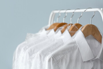 Rack with clean shirts in plastic bags on grey background