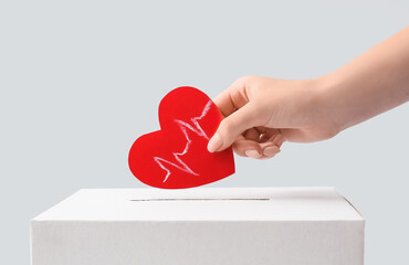 Woman holding red paper heart with cardiogram drawing and donations urn on light background, closeup