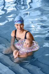 Young woman and her adorable baby with inflatable ring in swimming pool